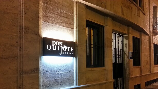 A building facade with a sign for "Don Quijote Hotel" illuminated in a window.