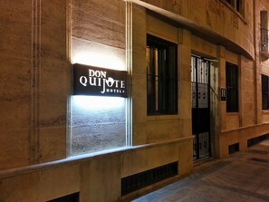 Fachada de edificio con un letrero luminoso que dice "Don Quijote Hotel" en una ventana.