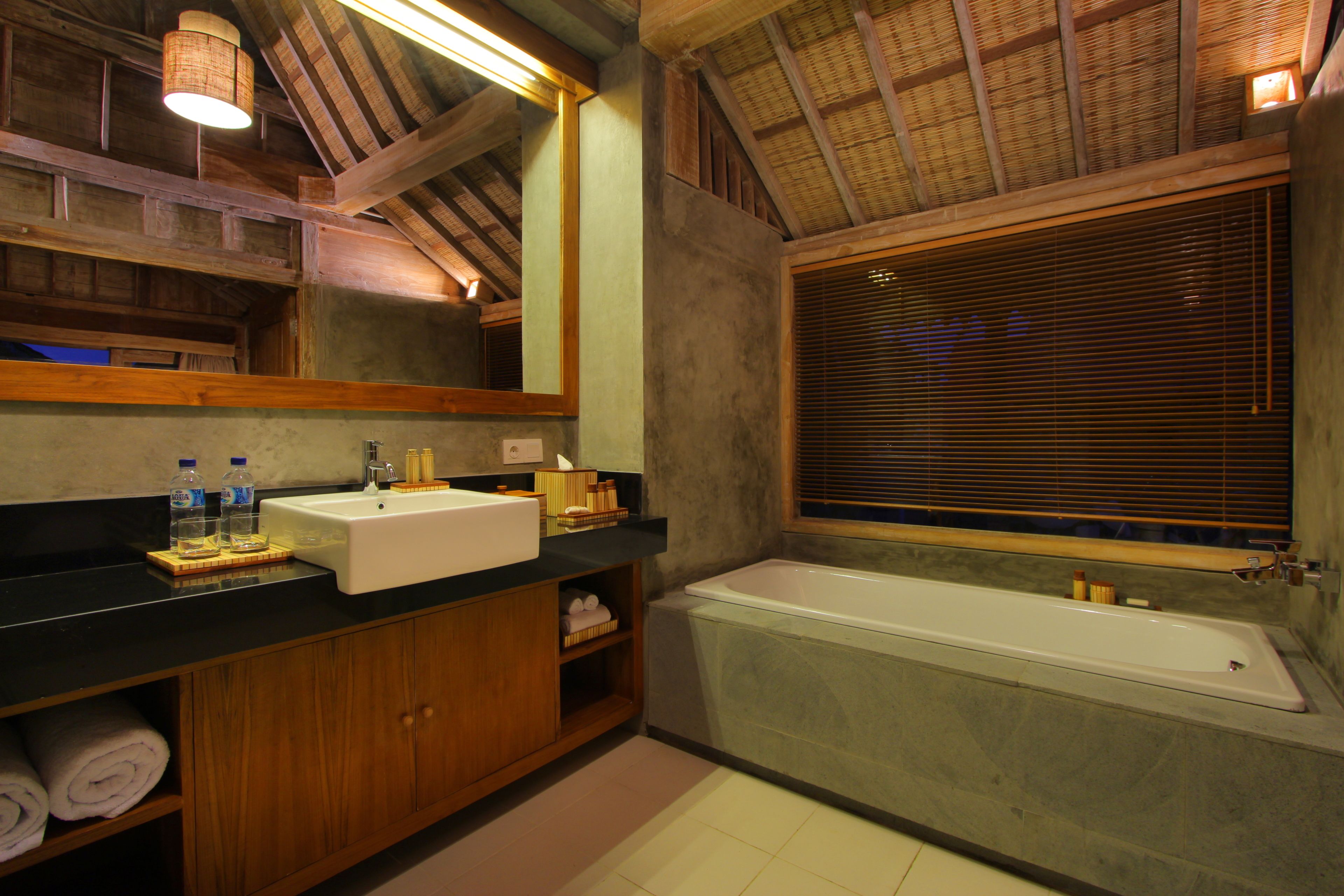 A bathroom with a wooden vanity, a large mirror, a bathtub, and a window with blinds.