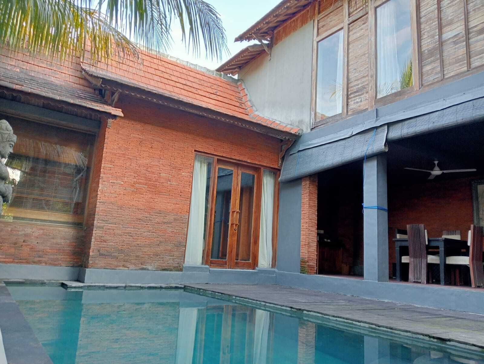 Una zona de piscina con una casa de ladrillo, una puerta de madera y un ventilador de techo.