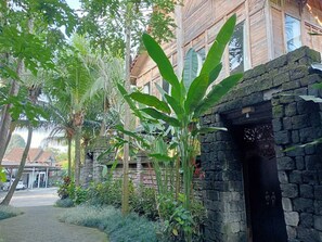 A traditional building with a stone entrance, surrounded by lush greenery and palm trees. - Suarti Boutique Village (Ubud)