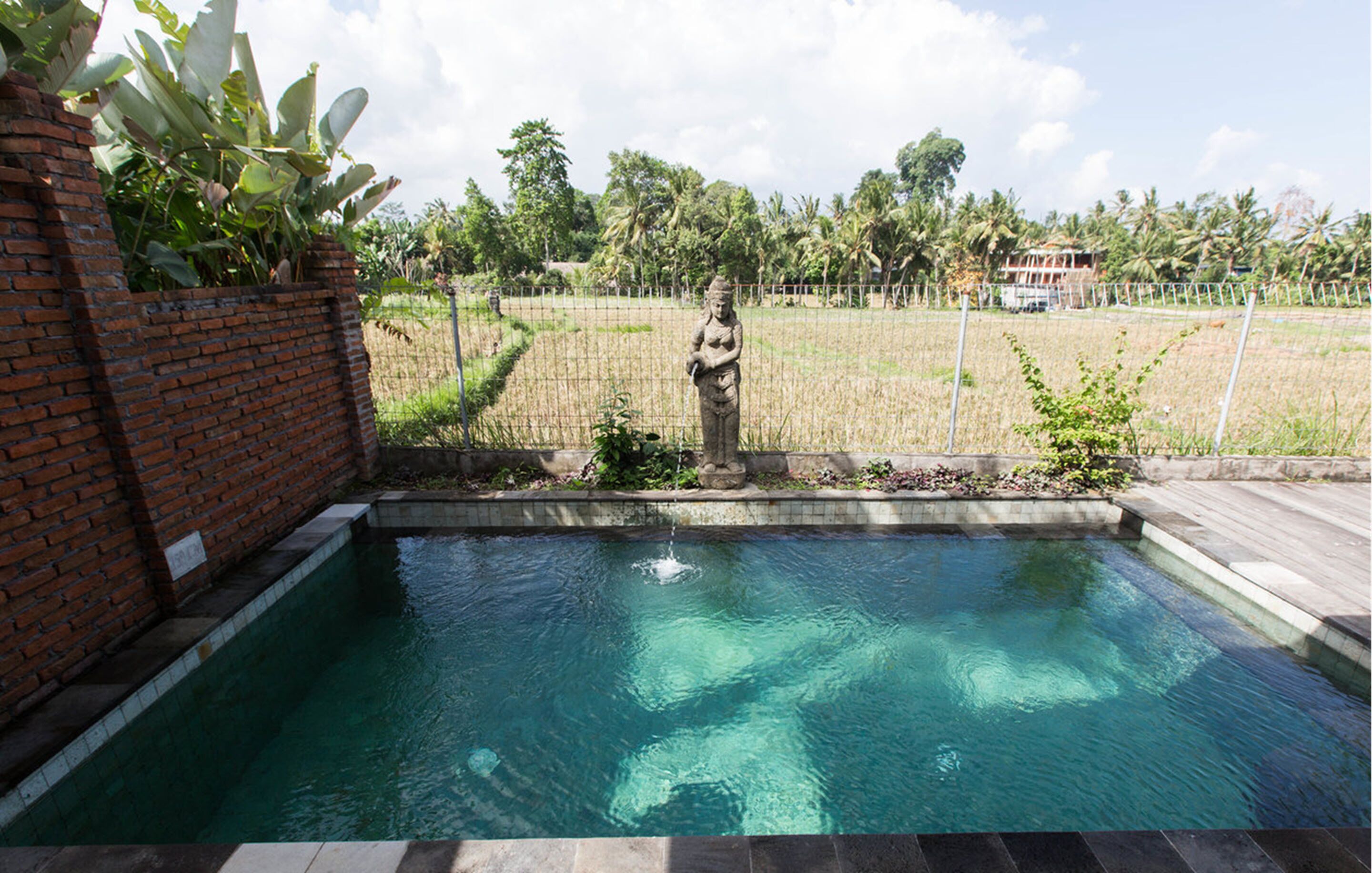 A swimming pool with a statue, surrounded by a brick wall and a fence.