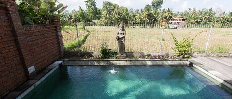 A swimming pool with a statue, surrounded by a brick wall and a fence.