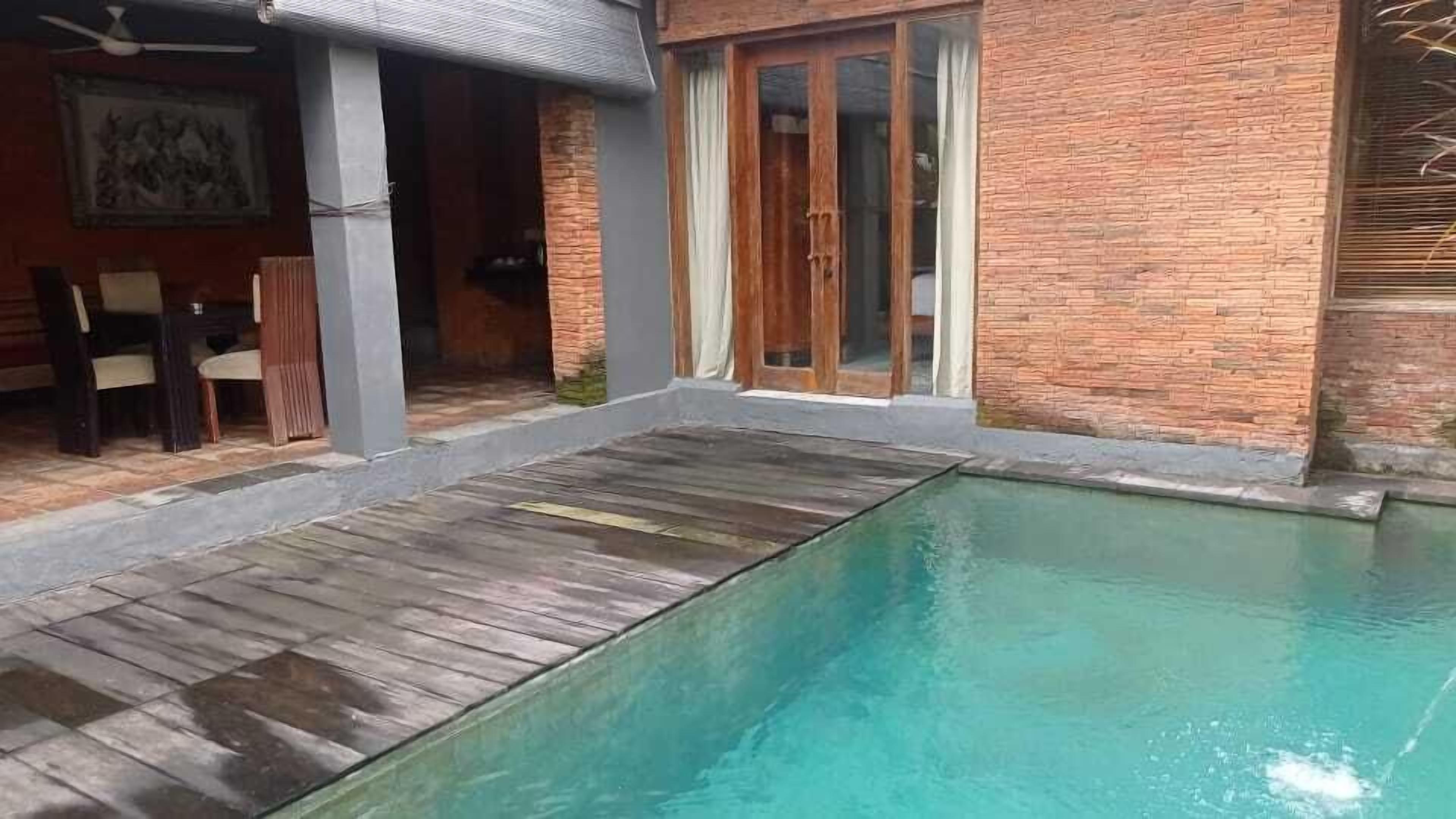 Une piscine dotée d’une terrasse en bois et d’un mur en briques.