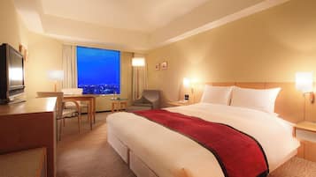 Une chambre d’hôtel avec un grand lit, un bureau, une chaise, une télévision et une vue sur la ville la nuit.