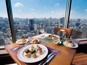 A dining table with plates of food and wine glasses, set against a cityscape view from a high-rise building. - Tokyo Dome Hotel (Tokyo)