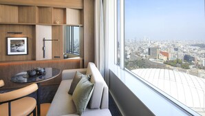 A modern hotel room with a city view, a sofa, a small table with a teapot, and a framed picture on the wall. - Tokyo Dome Hotel (Tokyo)