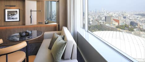 Una habitación de hotel moderna con vistas a la ciudad, un sofá, una mesita con tetera y un cuadro en la pared.