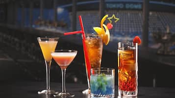 Vier verschiedene Cocktails auf einer Bar, im Hintergrund eine Stadiontribüne.