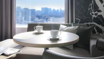 A modern hotel room with a round table, two white cups, and a city view through large windows.