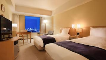 A hotel room with two beds, a desk, a television, and a view of a cityscape at night.