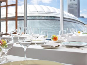 Una mesa de comedor dispuesta con copas de vino y platos, con vista al Tokyo Dome al fondo.