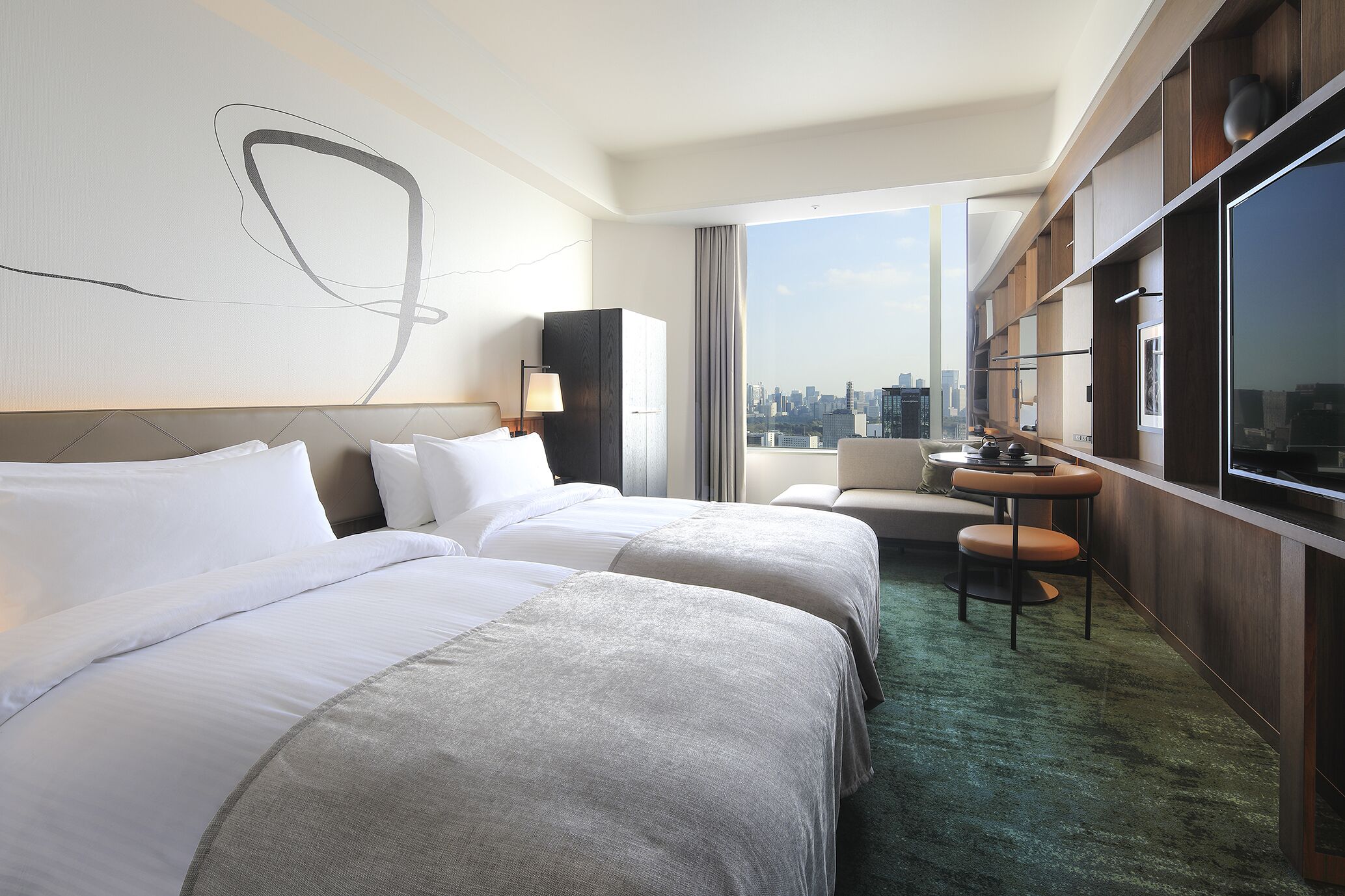 Habitación de hotel con dos camas, vistas a la ciudad, un escritorio con silla y un ventanal grande.