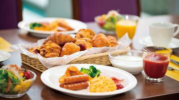 A breakfast table with croissants, sausages, scrambled eggs, and a glass of orange juice.