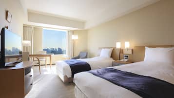 A hotel room with two beds, a desk, a TV, and a city view.