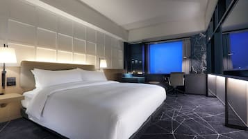 A modern hotel room with a large bed, bedside lamps, a desk, and a view of the city at night.