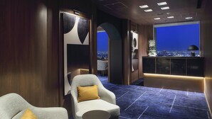 A modern hotel room with a city view, a large window, a seating area with two armchairs, and a dark blue carpet. - Tokyo Dome Hotel (Tokyo)