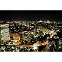 A nighttime cityscape with illuminated buildings and a highway.