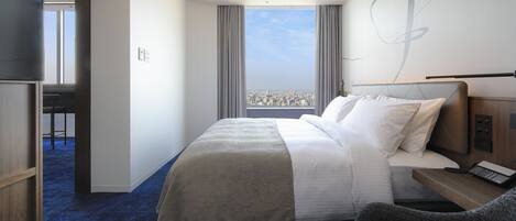 A modern hotel room with a large bed, a desk with a phone, and a view of the city through large windows.