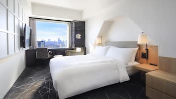 A hotel room with a large bed, a desk, a chair, a TV, and a view of the city skyline.
