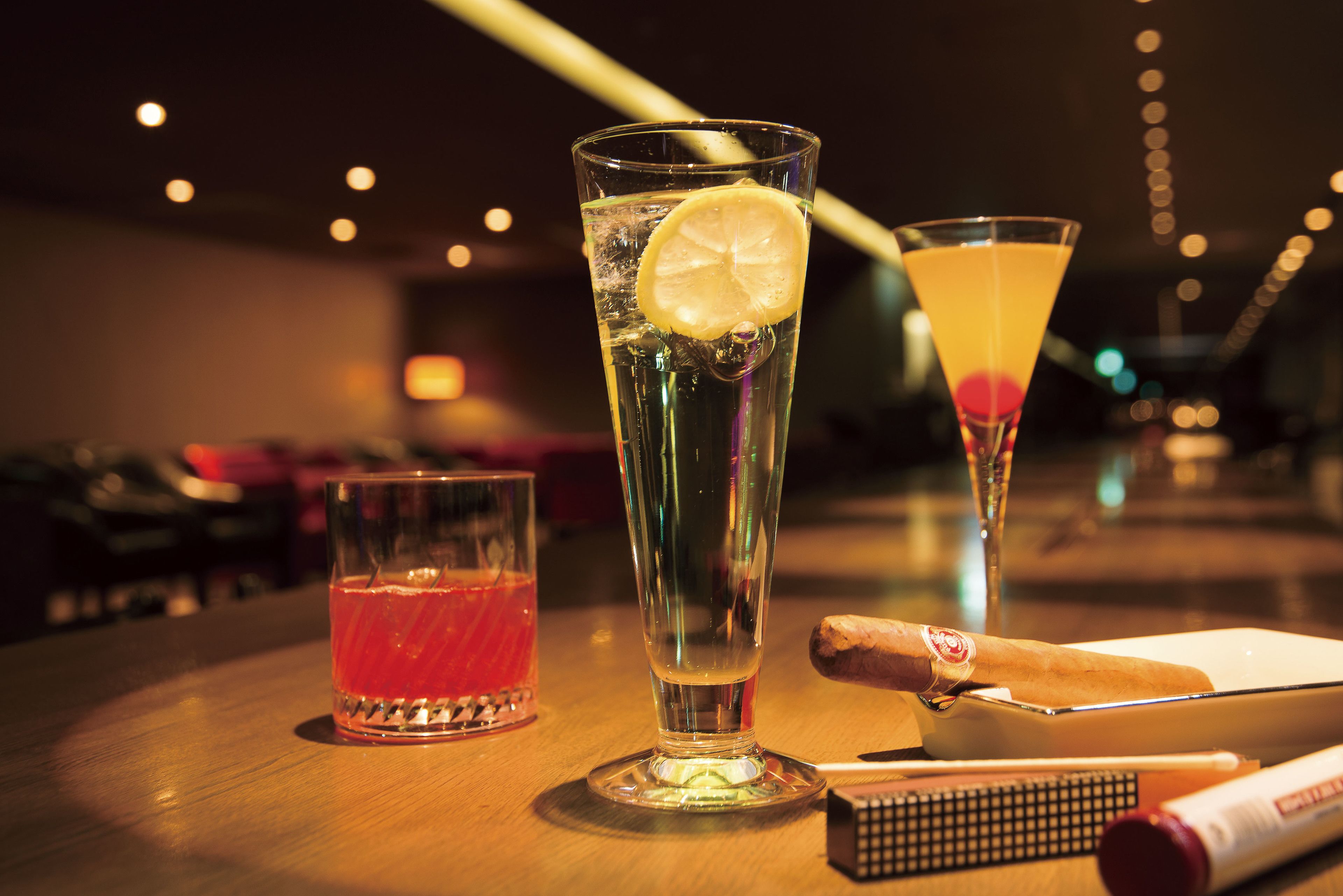 A bar setting with two glasses of beverages, one with a lemon slice, and a bottle of champagne.