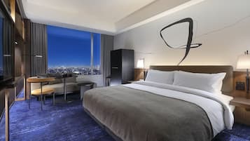 A modern hotel room with a large bed, a desk, and a view of the city at night.