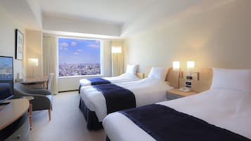 A hotel room with three beds, a desk, a chair, and a TV.