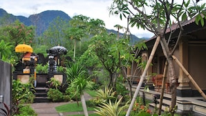 A garden pathway leading to a traditional building with a tiled roof, surrounded by lush greenery and a mountain backdrop. - Trijaya Guest House (Pemuteran)