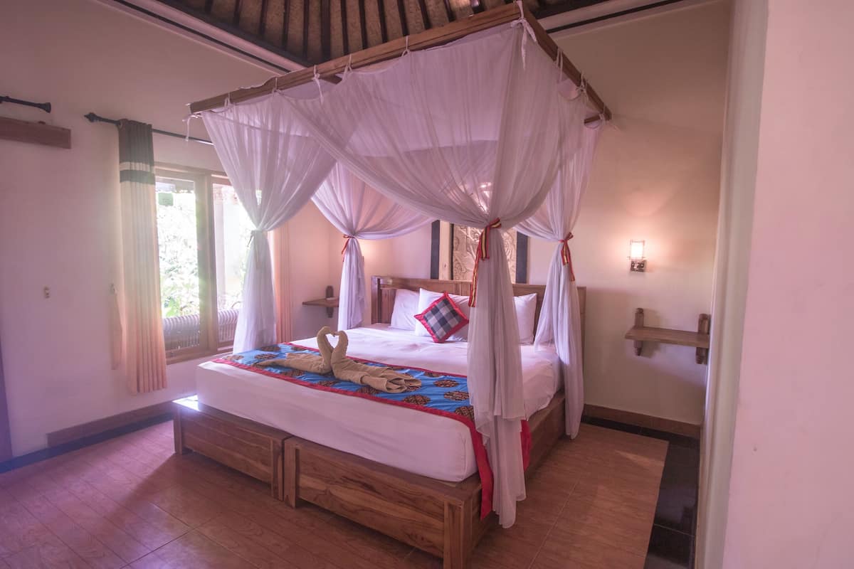 A four-poster canopy bed with a wooden base, white bedding, and a decorative pillow.