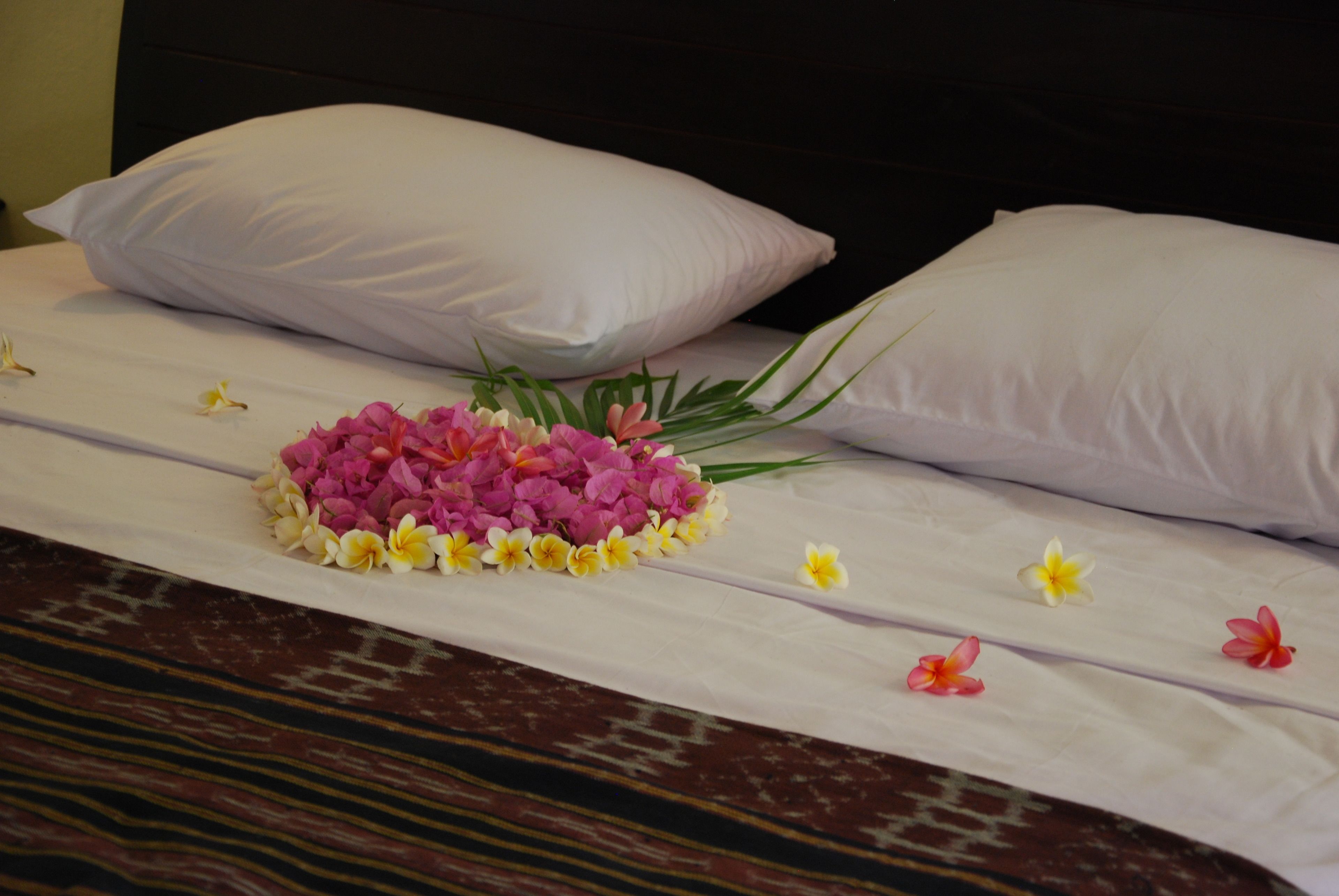 Una cama bien hecha con sábanas blancas, un centro de mesa floral y un cabecero oscuro.