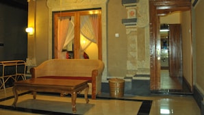 A lobby with a wooden sofa, a ceiling fan, a decorative mirror, and a tiled floor. - Trijaya Guest House (Pemuteran)