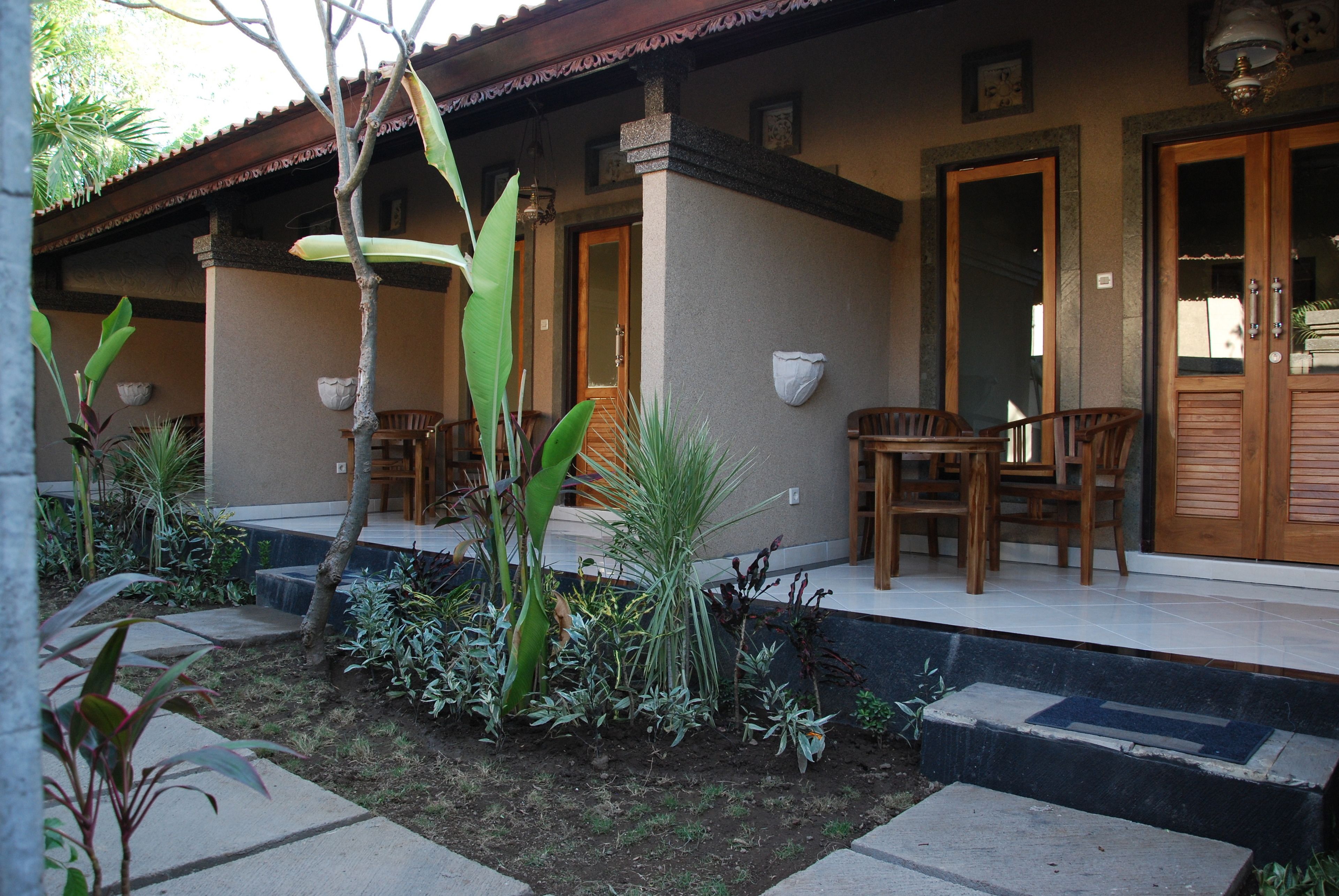 A covered outdoor area with a wooden table and chairs, surrounded by various plants and a small garden.