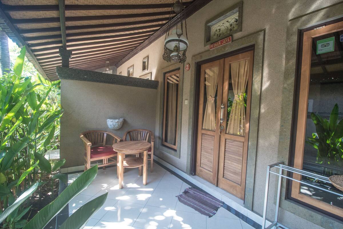 A covered outdoor area with a wooden table and chairs, a potted plant, and a door with a sign above it.