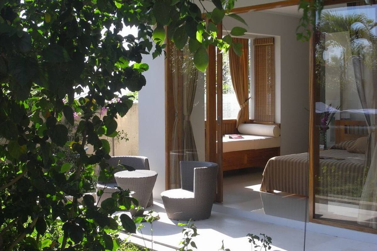 A bedroom with a large window, a bed, and a seating area with chairs.