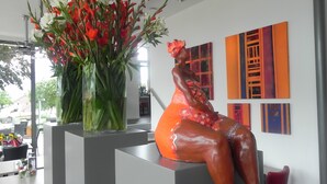 A modern interior with a sculpture of a woman in red, a tall vase with red and white flowers, and abstract paintings on the wall. - Hotel Restaurant Uit de Kunst (Vijlen)