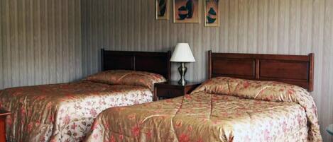 Une chambre d’hôtel avec deux lits, une table de chevet, une lampe et trois œuvres d’art accrochées au mur.