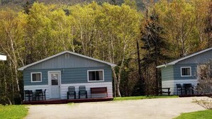 Two cabins with a paved driveway, outdoor seating, and a forested backdrop. - The Mountain View Motel & Cottages (Pleasant Bay)