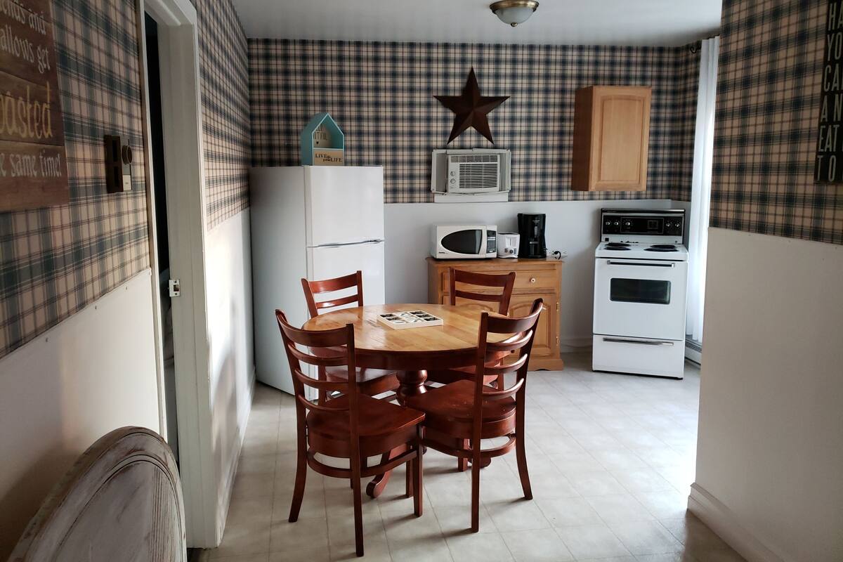A compact kitchen with a dining table, chairs, a refrigerator, microwave, coffee maker, and a stove.