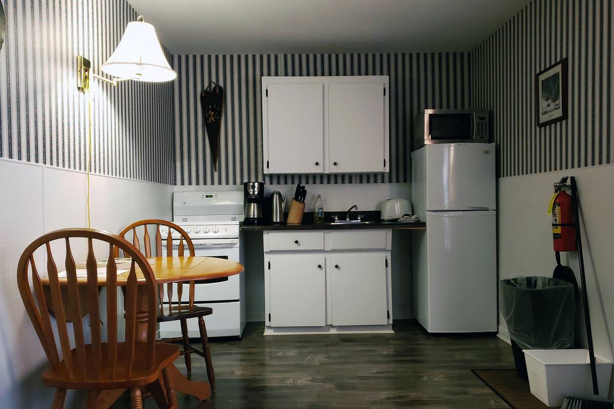 A compact kitchen with white cabinets, a microwave, a stove, and a sink. There is a wooden dining table with chairs.