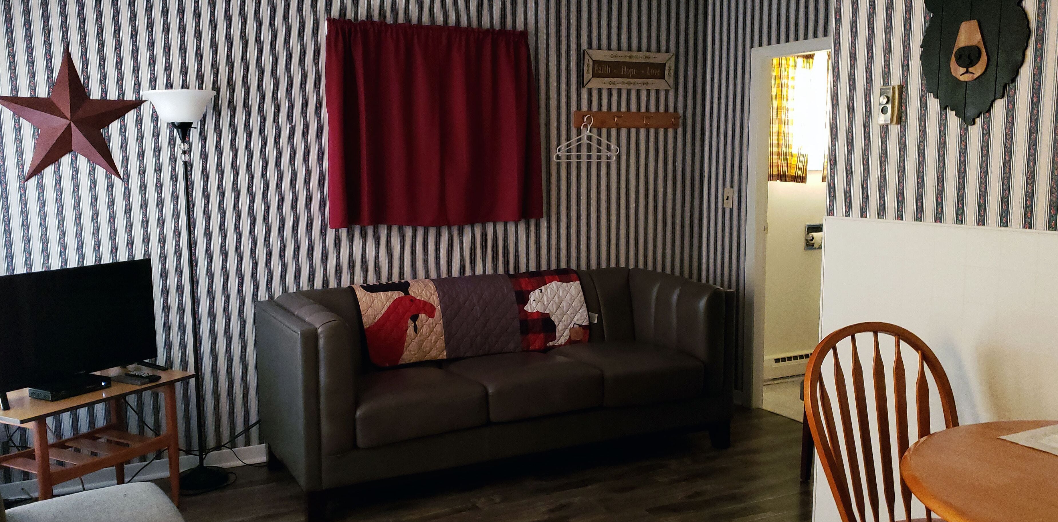Una sala de estar con papel tapiz a rayas, una decoración de estrella, una cortina roja, un perchero de madera y un televisor sobre un mueble de madera.
