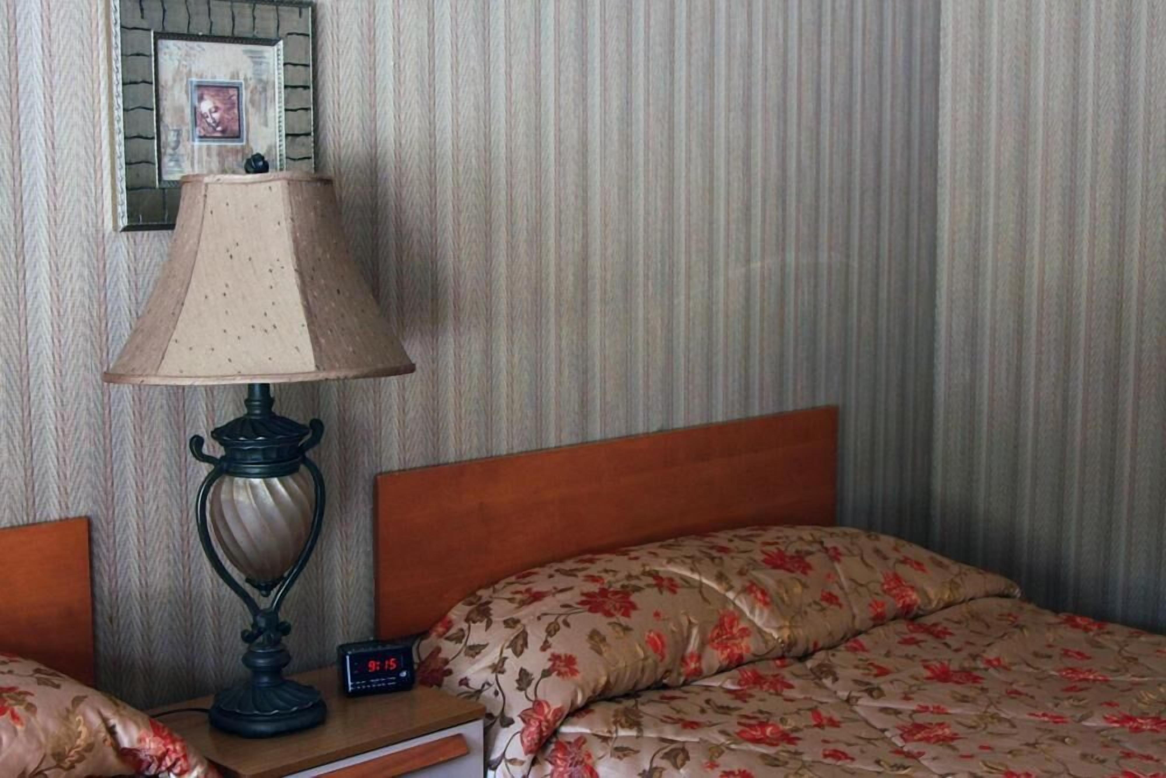 Une chambre d’hôtel avec un lit, une table de chevet avec une lampe, une horloge et un tableau encadré au mur.