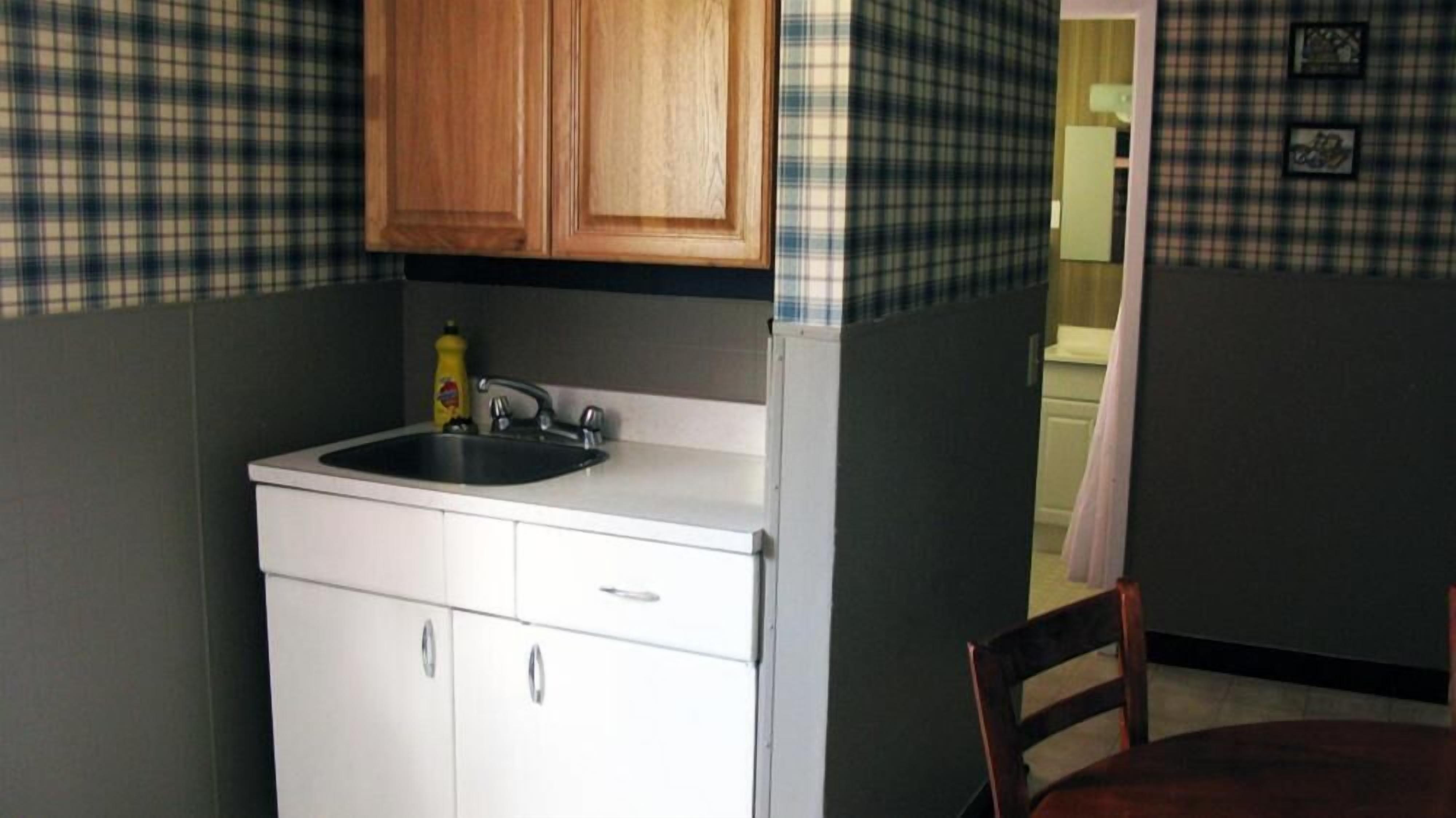 A compact kitchen with a sink, wooden cabinets, and a plaid-patterned backsplash.