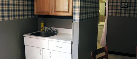A compact kitchen with a sink, wooden cabinets, and a plaid-patterned backsplash.