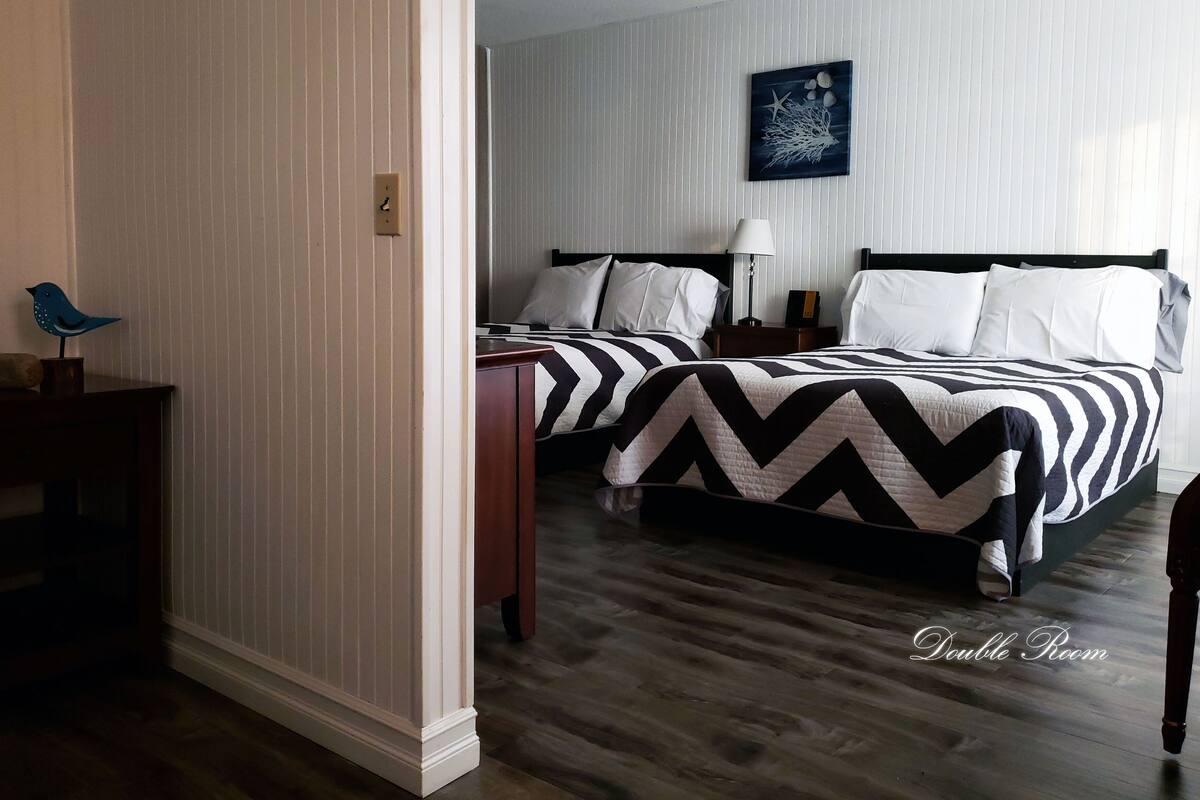 A double room with two beds, a nightstand, a lamp, and a wall-mounted artwork.