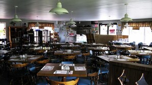A restaurant with multiple tables and chairs, hanging green pendant lights, and a counter area. - The Mountain View Motel & Cottages (Pleasant Bay)