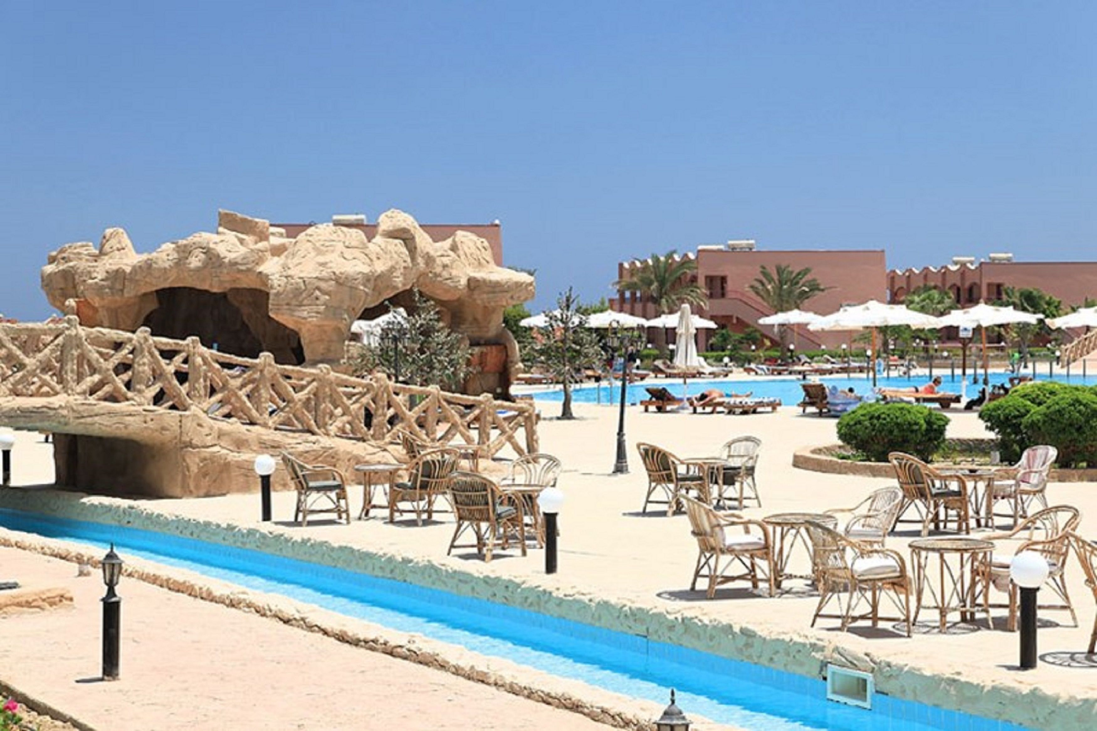 A poolside area with wicker furniture, a rock formation, and a clear blue sky.