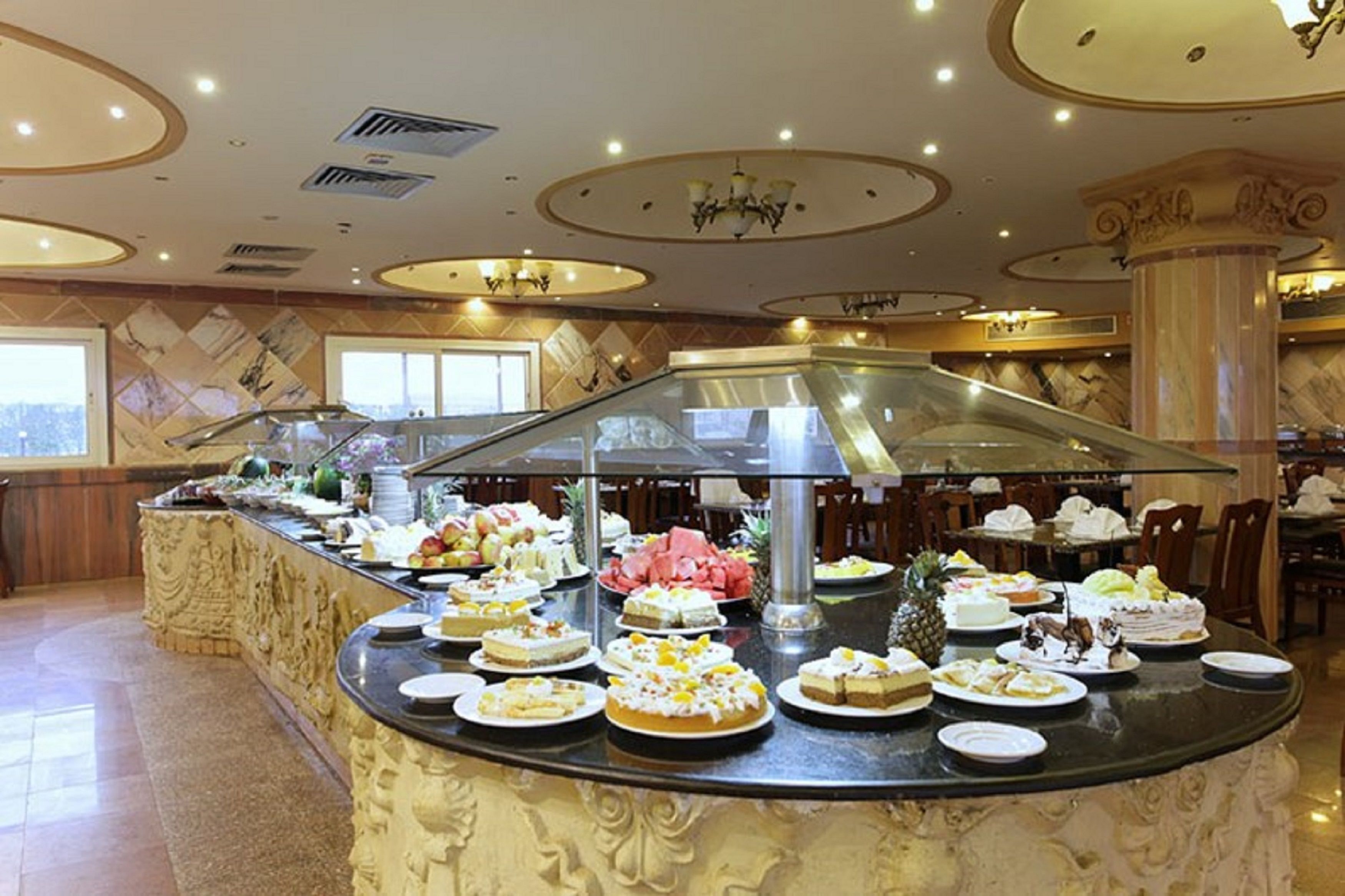 Ein Buffetbereich mit verschiedenen Desserts und Früchten, eine Glastrennwand und eine Marmorsäule.