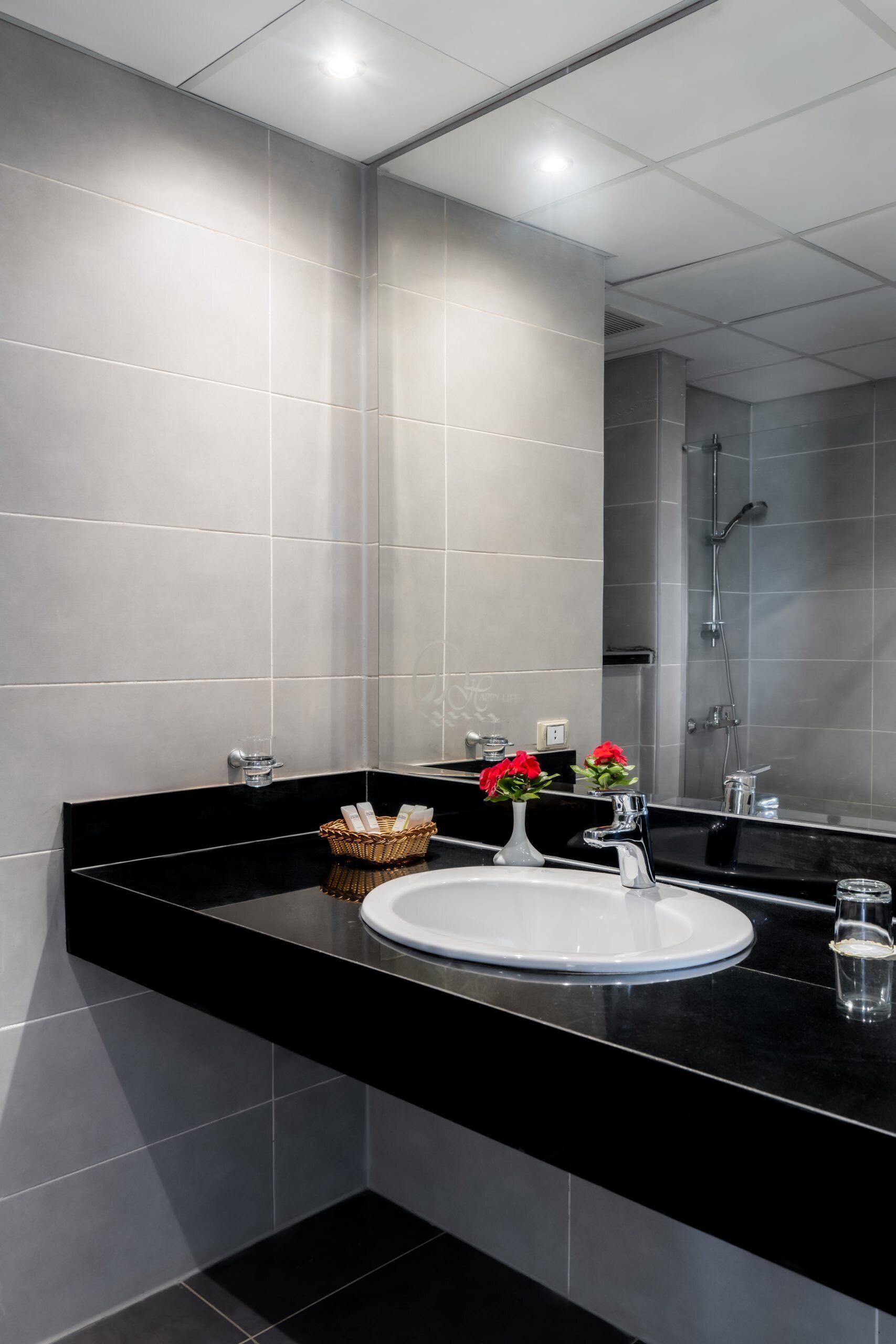 Een moderne badkamer met een zwart aanrecht, een witte wastafel en een grote spiegel.