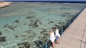A wooden pier extending into clear turquoise waters with rocky formations visible beneath the surface. - Three Corners Happy Life Beach Resort - All Inclusive (Marsa Alam)