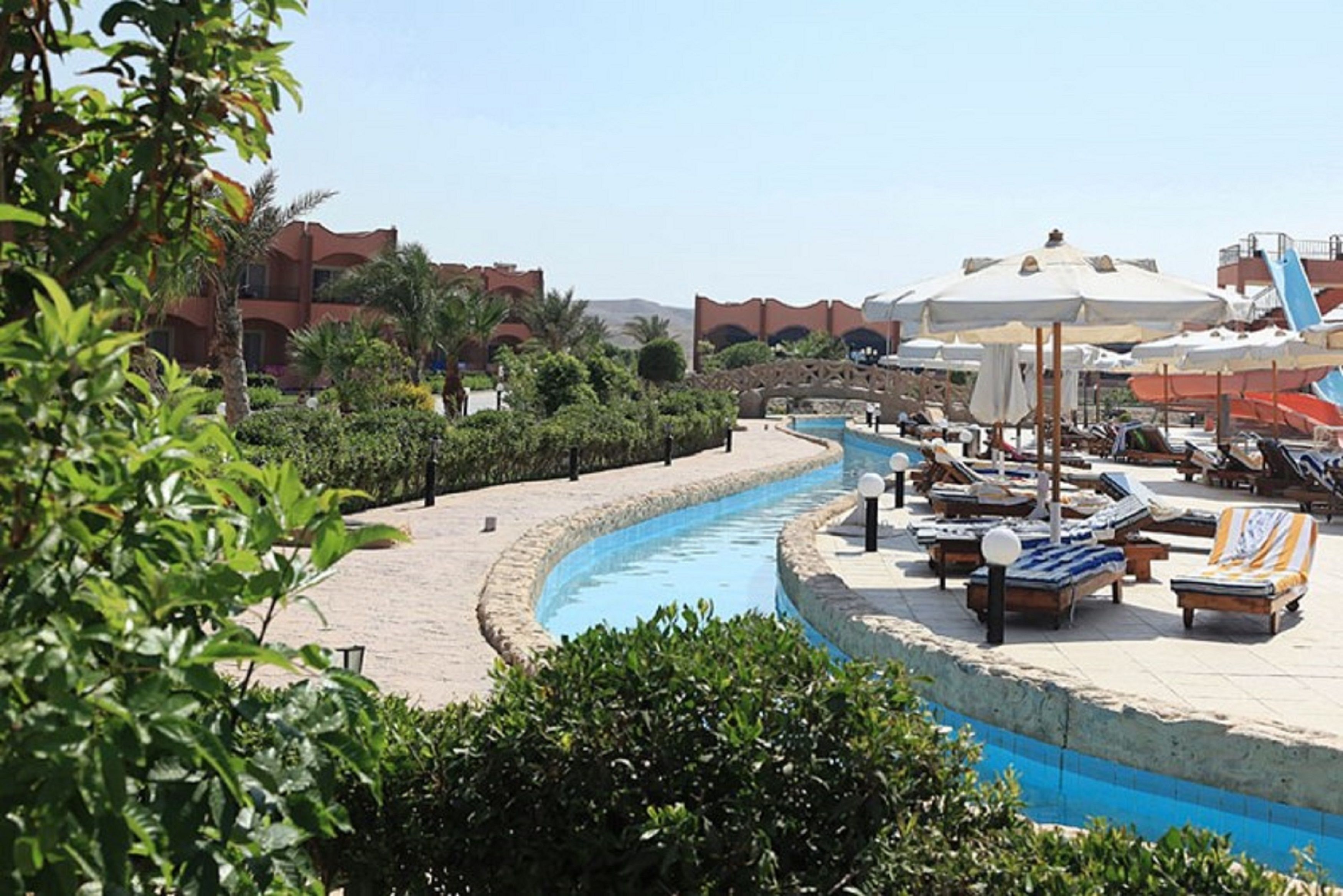 A poolside area with lounge chairs and umbrellas, surrounded by greenery and buildings.